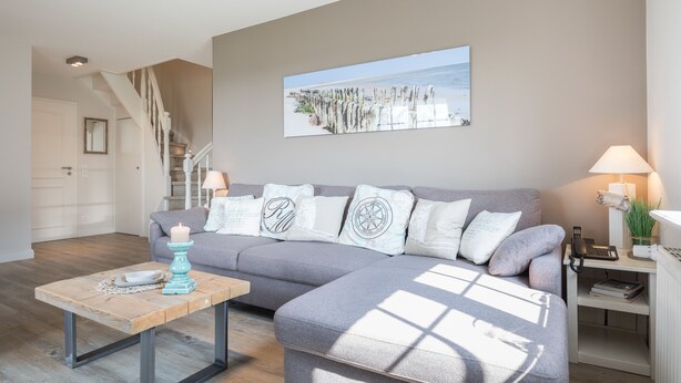 A modern living room with a grey sectional sofa, a wooden coffee table, a staircase, and a framed beach photograph on the wall. - Bestlage Zwischen Dorfteich & Dünen. Traumhaftes Landhaus im Friesenstil (Wenningstedt-Braderup (Sylt))
