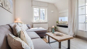 A cozy living room with a sectional sofa, a wooden coffee table, and a large window with curtains. - Bestlage Zwischen Dorfteich & Dünen. Traumhaftes Landhaus im Friesenstil (Wenningstedt-Braderup (Sylt))