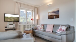 A living room with a sofa, a television, a radiator, and a window with curtains.