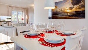 A dining area with a white table set for six, red placemats, and a sunset painting on the wall.