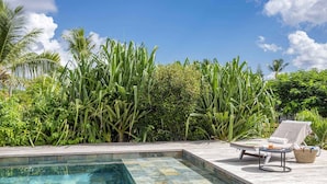 Uma área de piscina com uma espreguiçadeira e uma mesinha, rodeada por vegetação exuberante e um céu azul límpido.