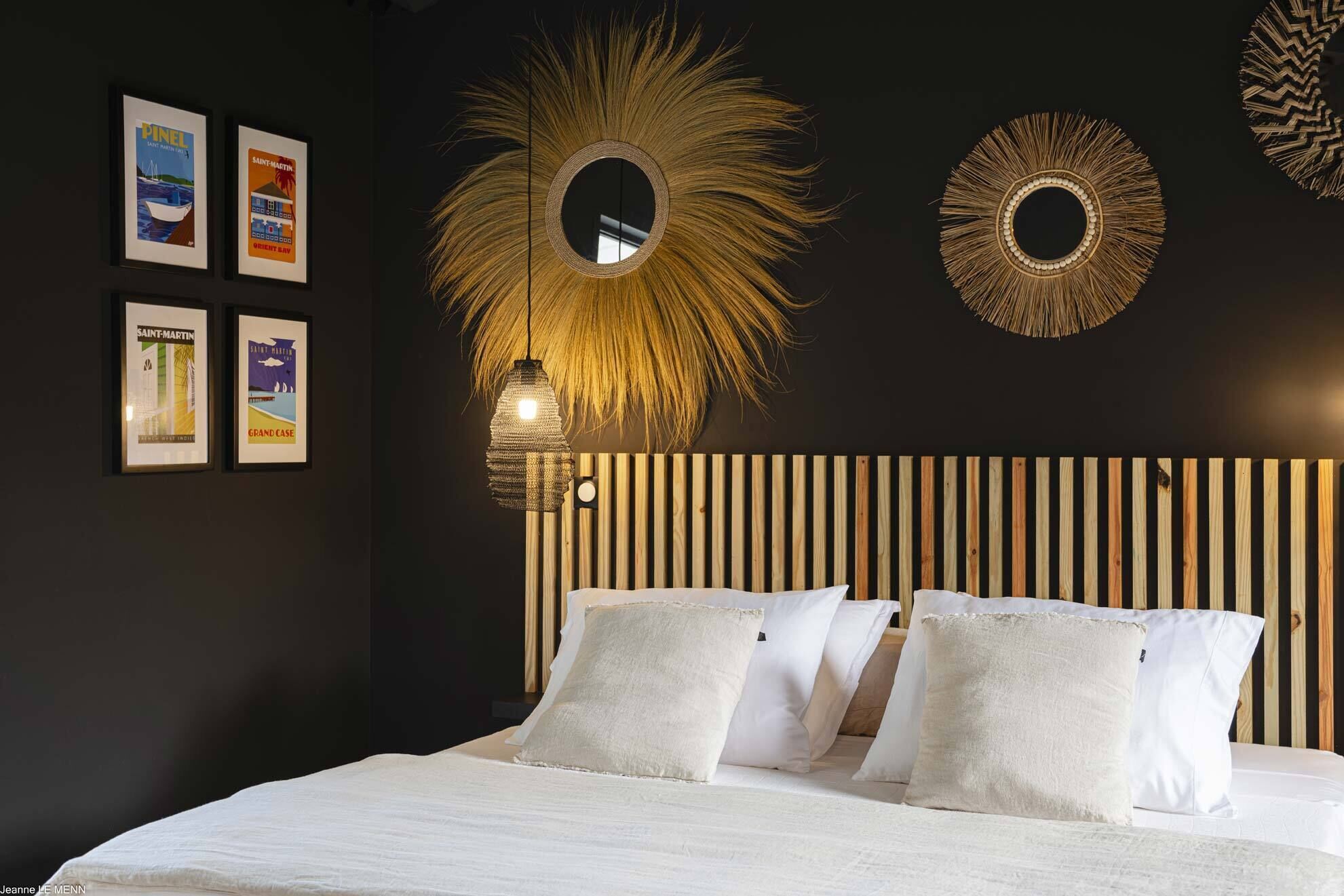 Un dormitorio con una cama, almohadas blancas, cabecera de listones de madera y espejos montados en la pared.