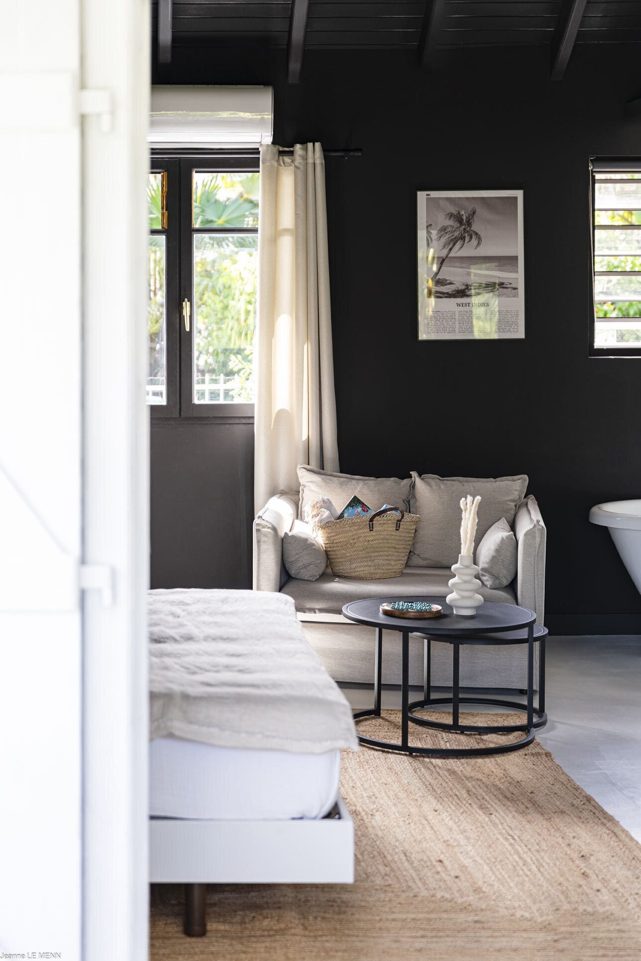 A modern bedroom with a bed, a sofa, a round coffee table, and a large window with curtains.