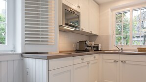 A modern kitchen with white cabinetry, a built-in oven, and a window with a view of greenery outside. - Feinster Sylt-luxus - Nantucket-style (Wenningstedt-Braderup (Sylt))