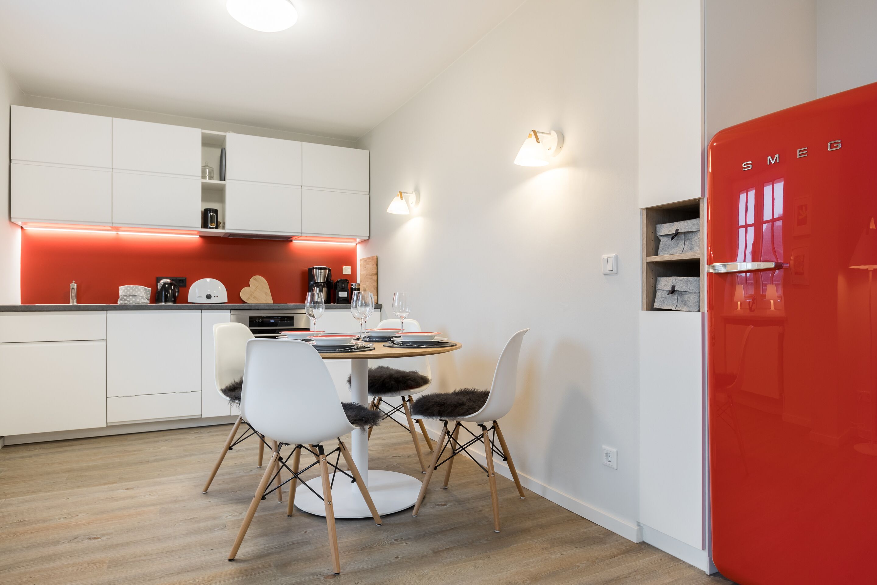 A modern kitchen with white cabinets, a red accent wall, and a red refrigerator.