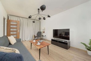 Un salon moderne avec un canapé, une table basse en bois, un téléviseur et un luminaire suspendu au plafond.