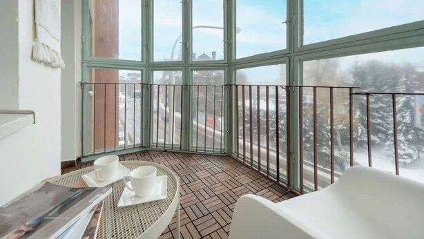 Ein Eckbalkon mit Blick auf eine verschneite Landschaft, ein Tisch mit Tassen und ein Sessel.