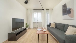 Ein modernes Wohnzimmer mit Flachbildfernseher, einer Couch, einem Couchtisch und einem großen Fenster mit Vorhängen.