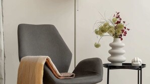 Ein moderner Sessel mit Überwurfdecke, einer Stehlampe und einem kleinen Tisch mit Blumen in einer Vase.