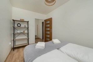 A bedroom with a bed, a shelf with items, and a door leading to another room.