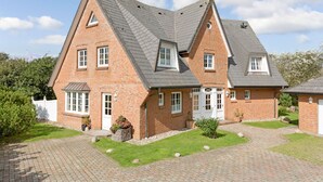 Une maison à deux étages, construite en briques, avec un toit à forte pente, une entrée principale dotée d’une porte blanche et une allée pavée menant à la porte d’entrée.