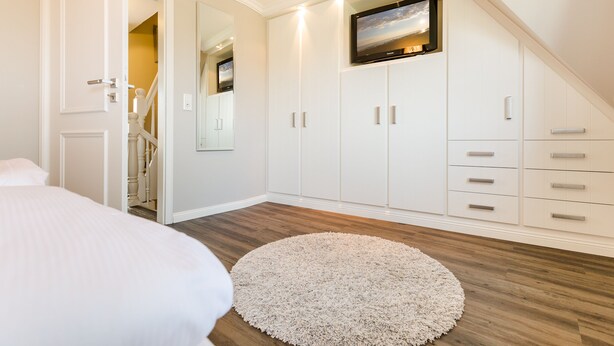 Une chambre avec un lit, un tapis rond, un téléviseur fixé au mur et un escalier menant à une autre pièce.