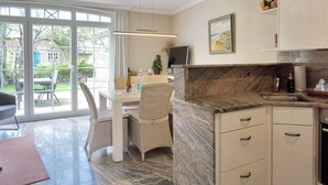 Une cuisine moderne dotée d’un plan de travail en marbre, de meubles blancs et d’un coin repas avec des chaises en osier.