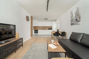 Un salon moderne comprenant un téléviseur, un canapé, un coin repas, une cuisine et des œuvres d’art accrochées au mur.
