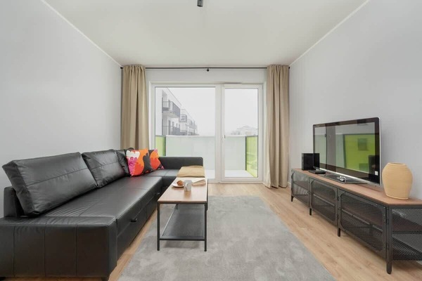 A living room with a modern design, featuring a TV, sofa, and large windows letting in natural light.