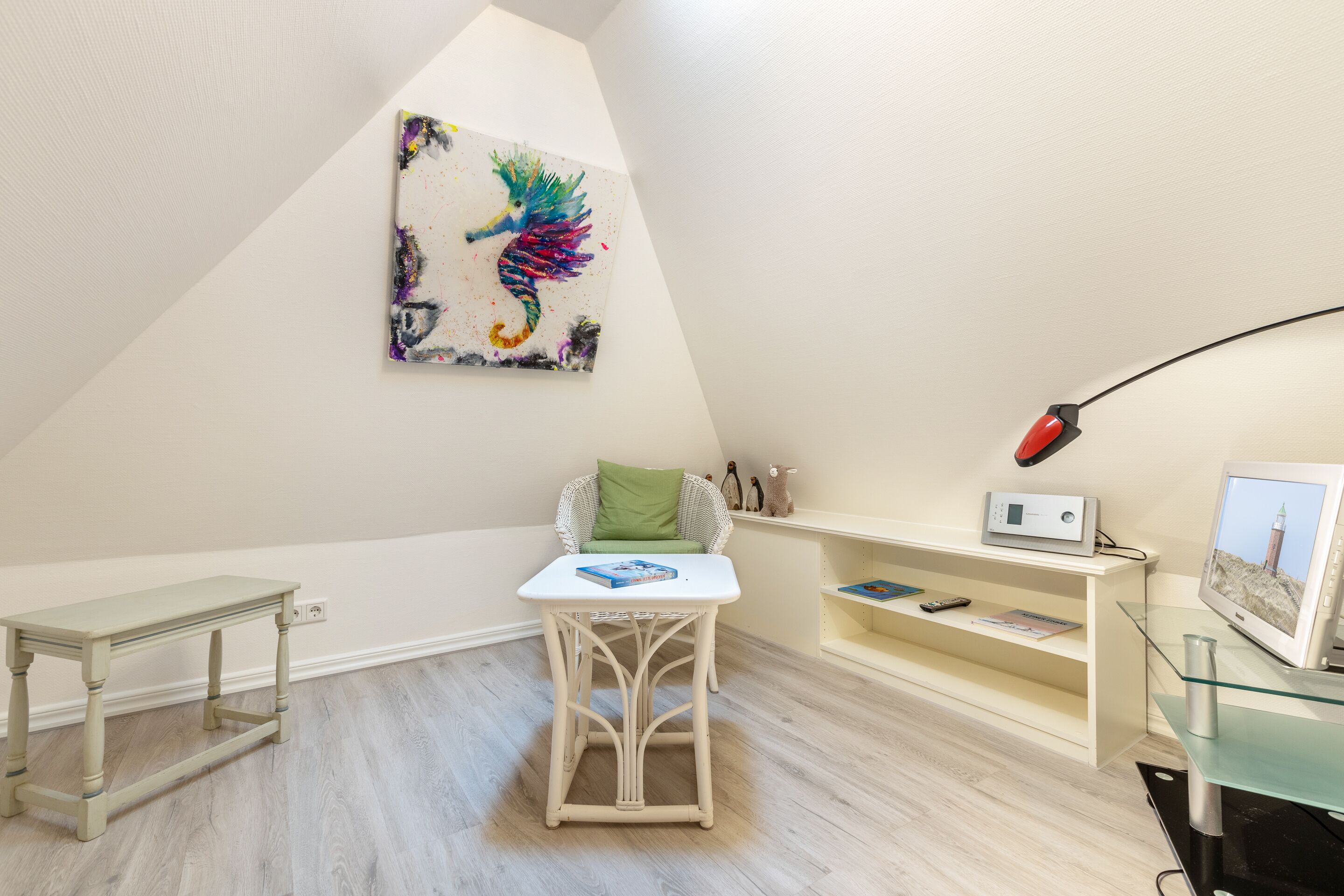 Een kamer met een witte tafel, een groene stoel, een kleurrijk kunstwerk aan de muur, een televisie en een lamp.