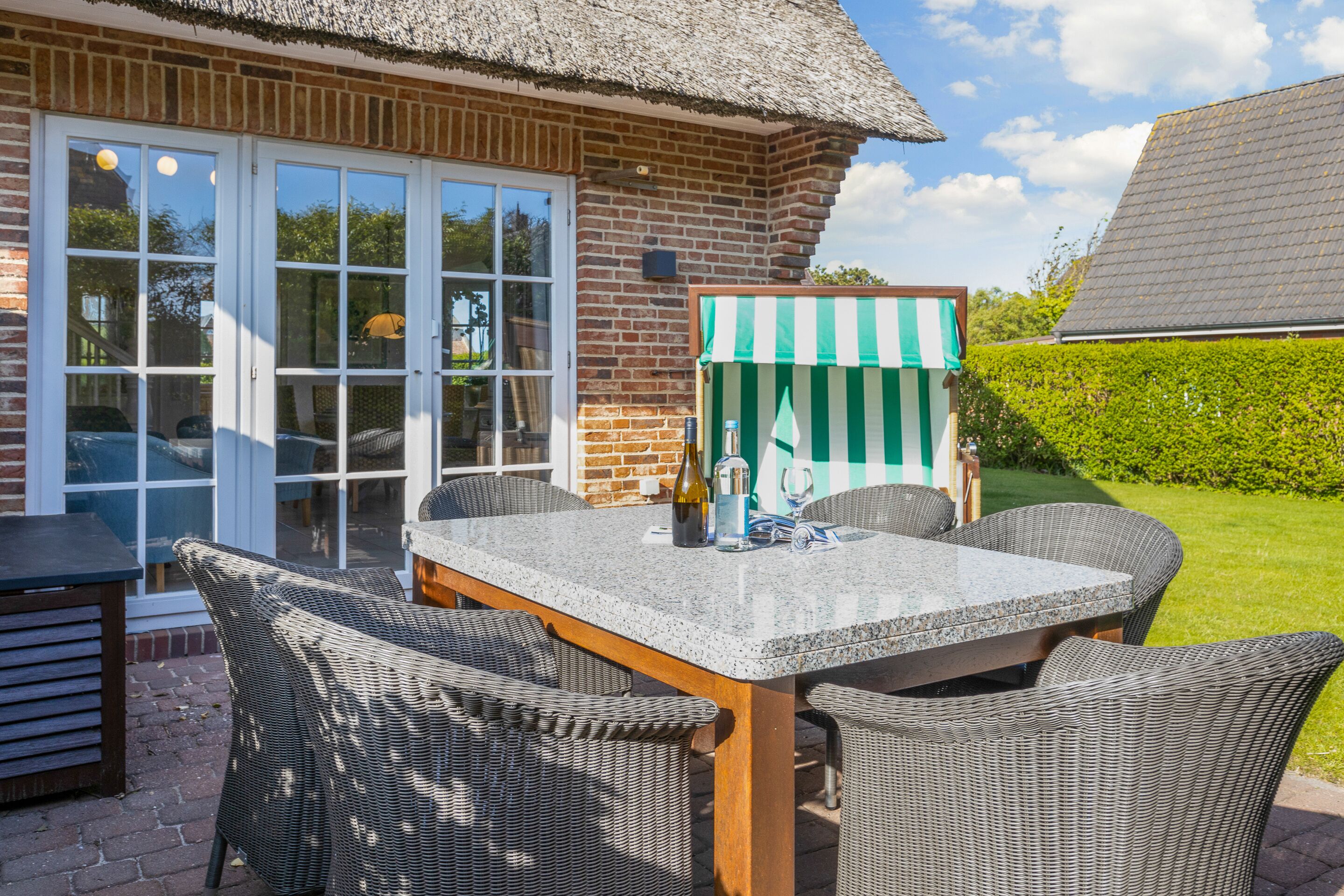Eine Terrasse mit Tisch und Stühlen, einem Reetdach und einem gestreiften Markisenvorzelt.