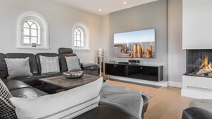 Una sala de estar moderna con un sofá modular, un televisor de pantalla plana, una chimenea y dos ventanas arqueadas.