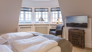Un dormitorio con una cama grande, televisión, un cofre de mimbre y vistas al exterior a través de un ventanal.