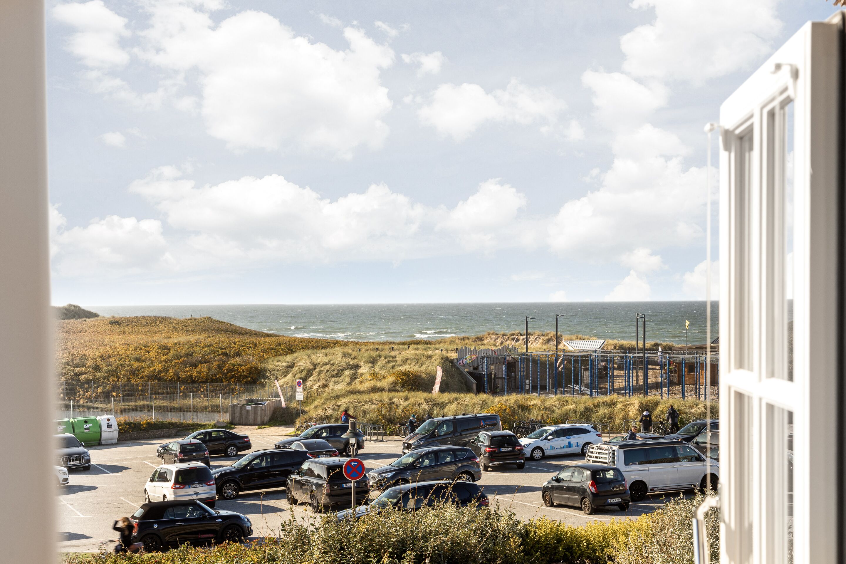 A parking lot with cars and a view of the beach and ocean.