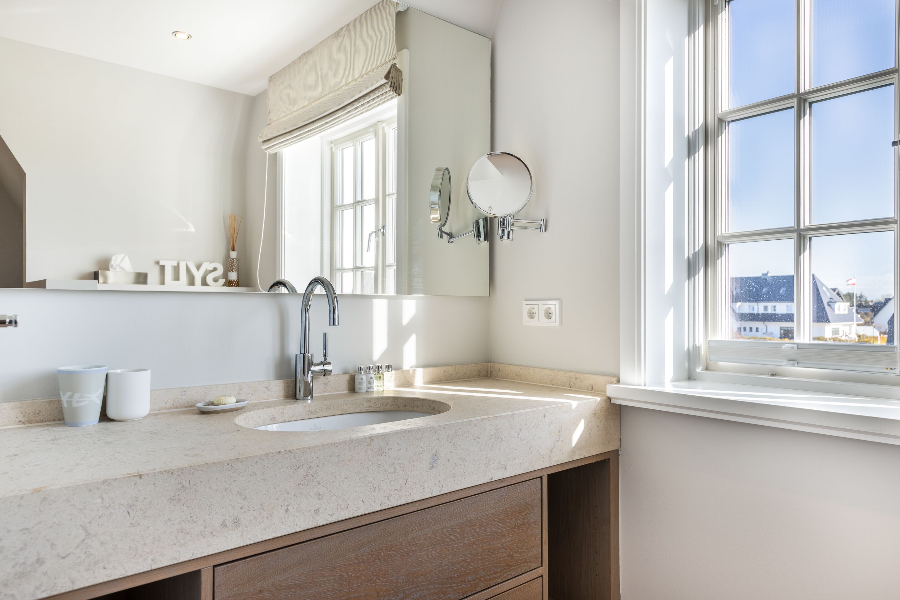 A bathroom with a large mirror, a sink, and a window.