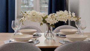 Une table à manger dressée avec de l’assiette blanche, des bols et un vase contenant des fleurs blanches.