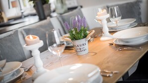 A dining table set with white plates, silverware, and a candle holder. A white vase with the text "FLEURS & PLANTES" holds purple flowers.