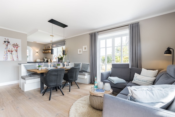 Una sala de estar moderna con un sofá gris, un comedor con mesa de madera y una cocina al fondo.