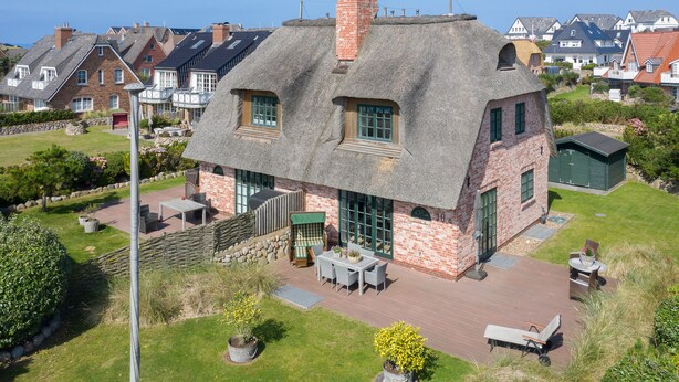 A thatched-roof house with a brick exterior, a patio with outdoor furniture, and a well-maintained garden.