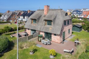 Una casa con techo de paja y fachada de ladrillo, un patio con mobiliario exterior y un jardín bien cuidado.