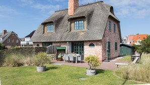 A traditional brick house with a thatched roof, a small garden with potted plants, and a patio with outdoor furniture.