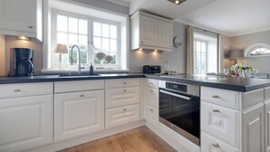 A modern kitchen with white cabinetry, a built-in oven, and a coffee maker. - Lifestyle Unter Reet, Strand & Meer um die Ecke (Wenningstedt-Braderup (Sylt))