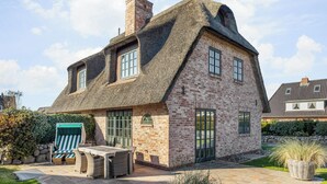 A brick house with a thatched roof, a patio with outdoor furniture, and a garden. - Lifestyle Unter Reet, Strand & Meer um die Ecke. Ihr Optimales Urlaubs-domizil (Wenningstedt-Braderup (Sylt))