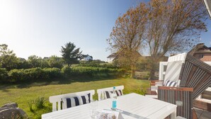 Een terras met een witte tafel en stoelen, een waterfles en een tijdschrift.
