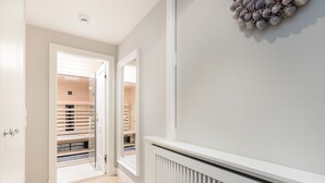 Een gang met een radiator, een spiegel en een deur die leidt naar een kamer met houten vloeren en jaloezieën.