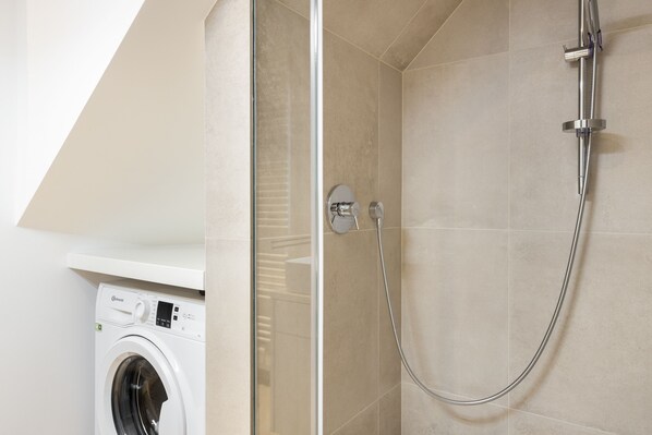 Een moderne badkamer met een glazen douchecabine, een ingebouwde wasmachine en beige tegels.