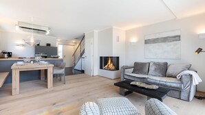 Ein modernes Wohnzimmer mit Kamin, einer Couch, einem Couchtisch und einem Essbereich mit Holztisch und Stühlen.
