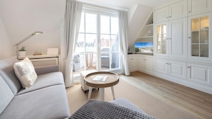 A modern living room with a sofa, a small round table, and a view of the outside through large windows. - Ferienwohnung im OG, DG, ca. 50m² Nutzfläche, 1 Parkplatz, Nichtraucher (Wenningstedt-Braderup (Sylt))