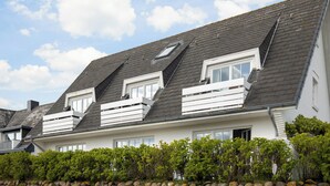 A two-story house with a sloped roof, dormer windows, and a stone wall in the foreground. - Ferienwohnung im OG, DG, ca. 50m² Nutzfläche, 1 Parkplatz, Nichtraucher (Wenningstedt-Braderup (Sylt))