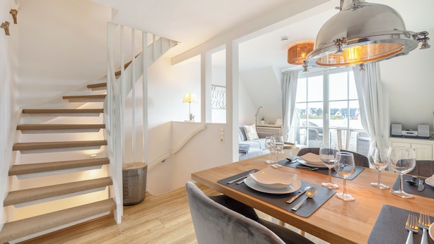 A dining area with a wooden table set for four, a staircase, and a view of the outdoors. - Ferienwohnung im OG, DG, ca. 50m² Nutzfläche, 1 Parkplatz, Nichtraucher (Wenningstedt-Braderup (Sylt))