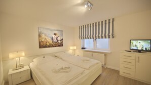 A hotel room with a large bed, two bedside tables with lamps, a television, a window with striped curtains, and a painting on the wall.