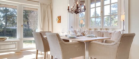 Een eetgedeelte met rieten stoelen, een houten tafel en een kroonluchter.