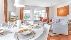 A dining area with a round table set for four, white walls, and a large window with curtains.