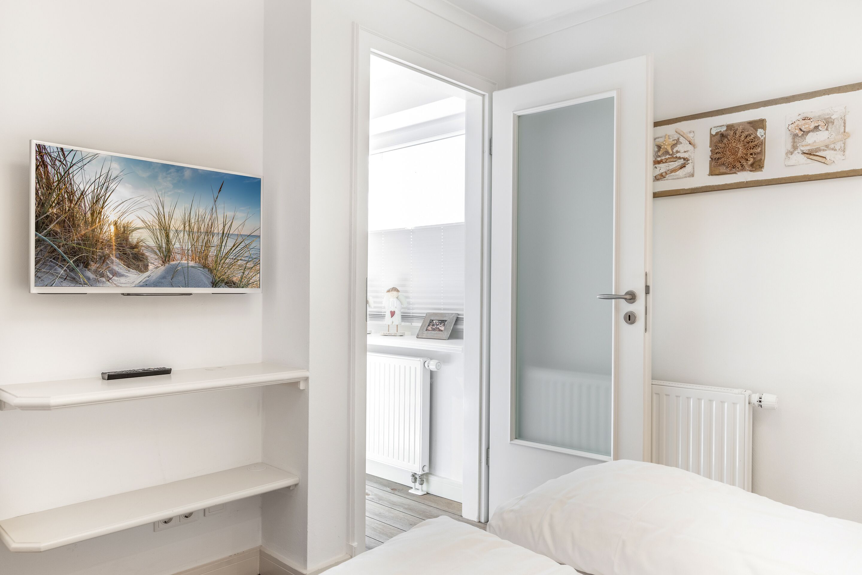 A bedroom with a bed, a TV on a shelf, a door leading to a balcony, and a wall with decorative items.