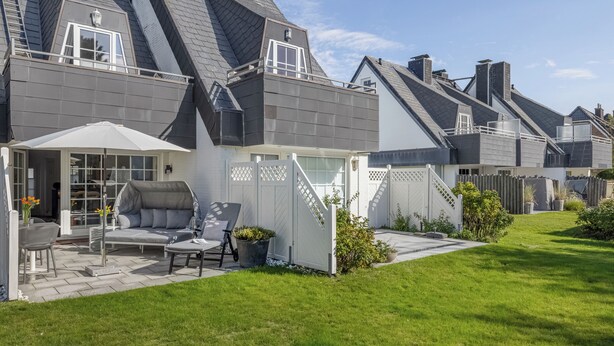 A residential house with a covered patio area, a lawn, and a white fence.