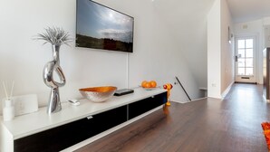 A modern living room with a flat-screen TV mounted on the wall, a white console table with a decorative vase, a bowl, and a small figurine.