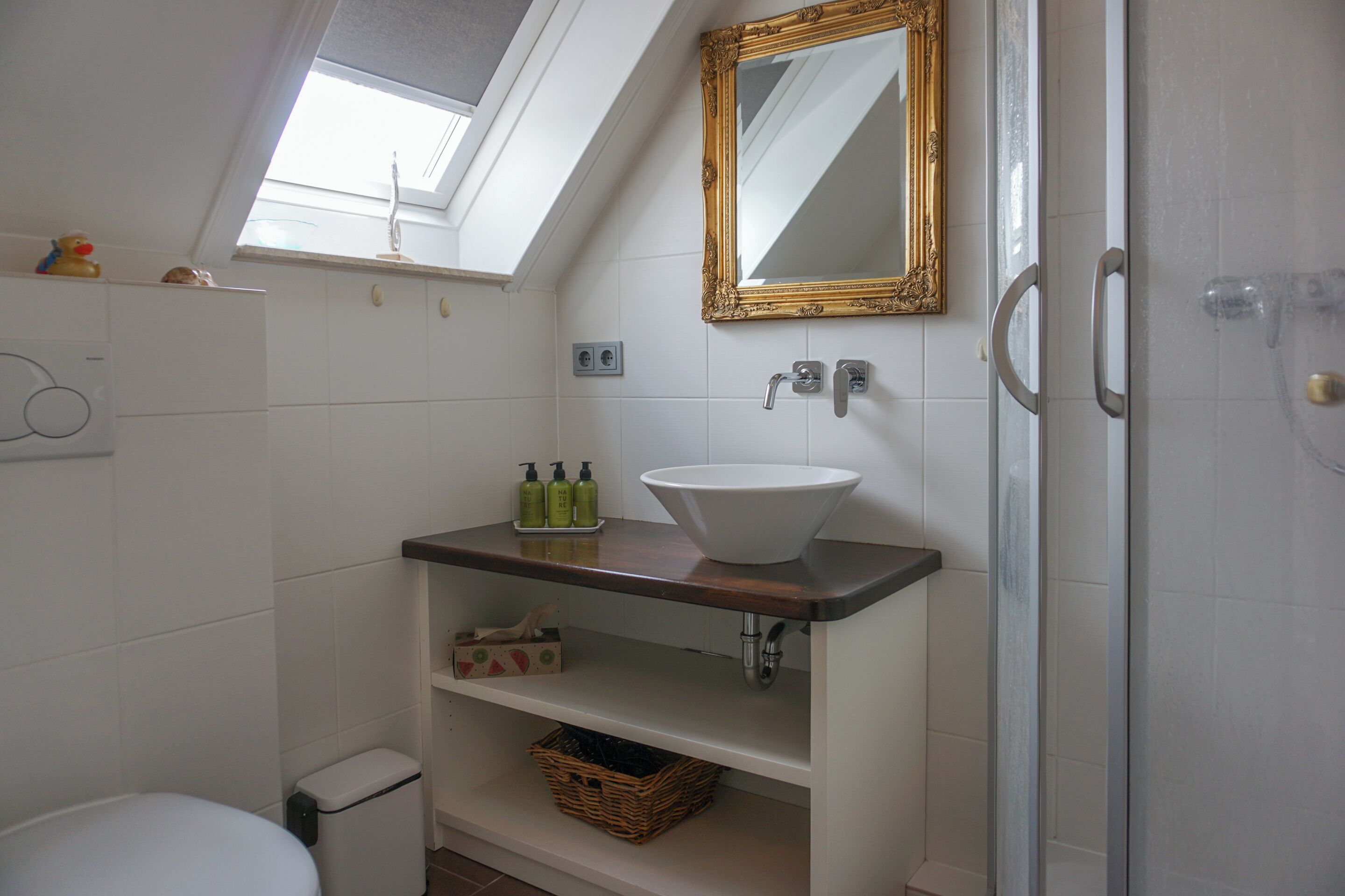 A bathroom with a skylight, a white sink, a gold-framed mirror, and a shower.
