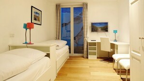 Ein Schlafzimmer mit einem Bett, einem Schreibtisch, einem Stuhl und einem Fenster mit Vorhängen.