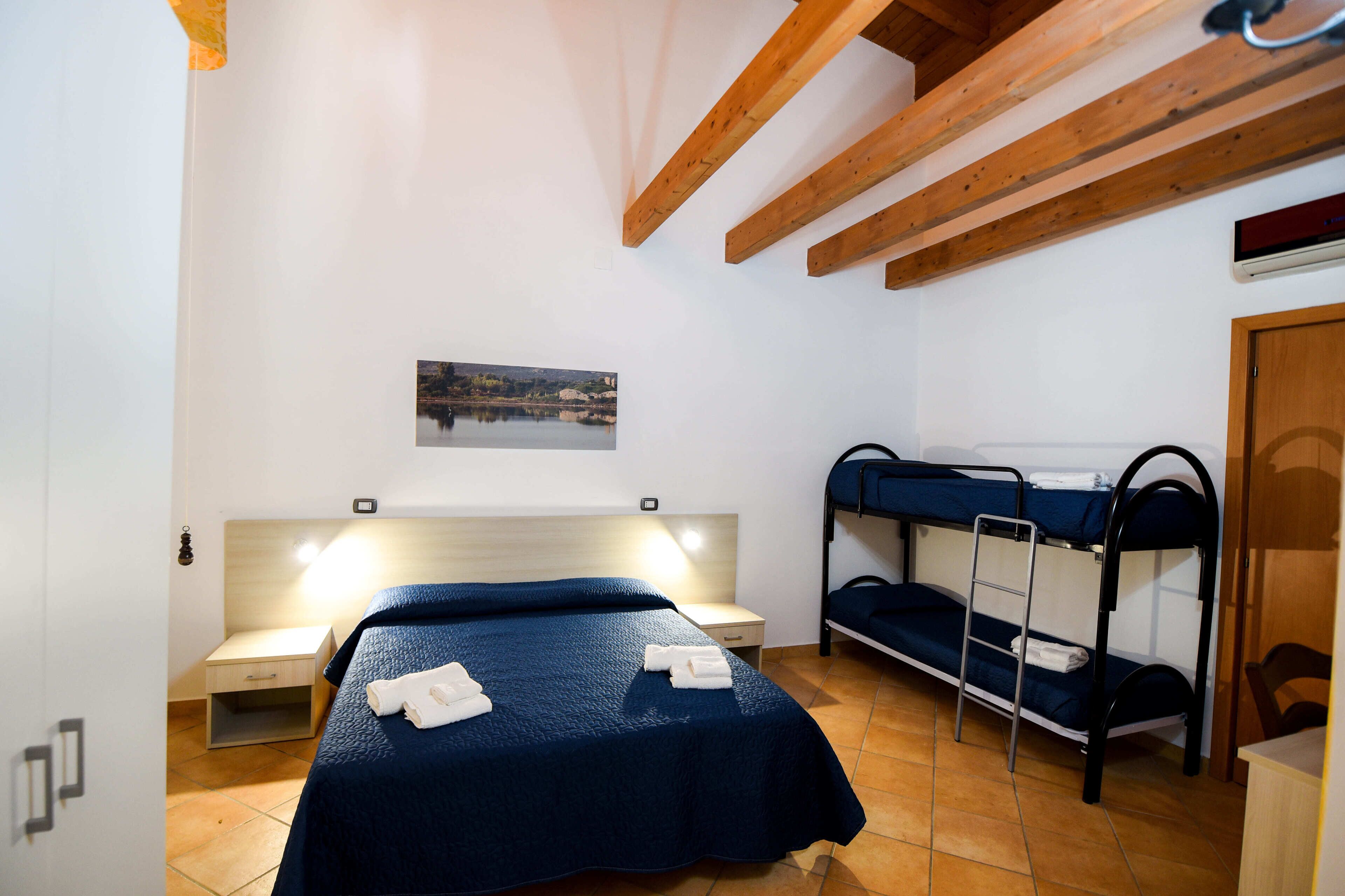 A room with a single bed, a bunk bed, a small desk, and a wall-mounted air conditioning unit.