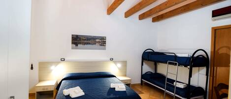 A room with a single bed, a bunk bed, a small desk, and a wall-mounted air conditioning unit.